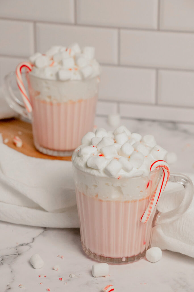 Homemade pink peppermint hot cocoa with crushed candy canes, whipped cream, and marshmallows side view